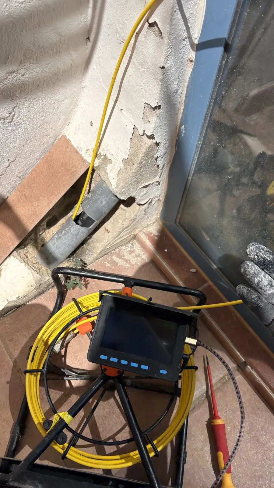 Carrete de cámara de videoinspección introducido en un tubo de desagüe junto a una pared con la pintura levantada por la humedad