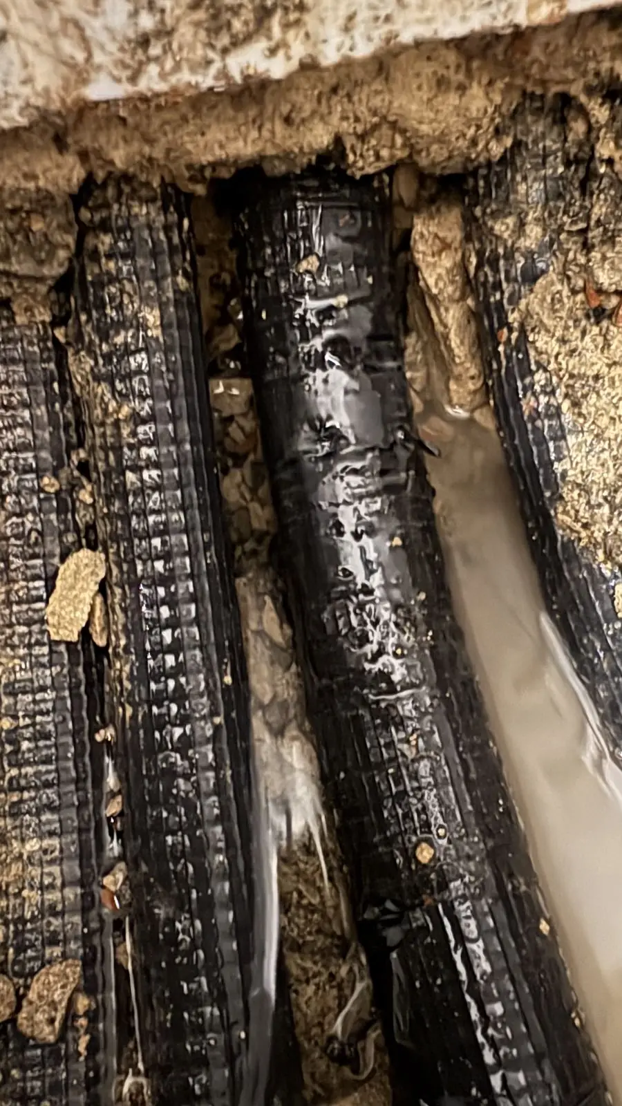 Tubos corrugados negros anegados de agua dentro de una roza bajo el suelo